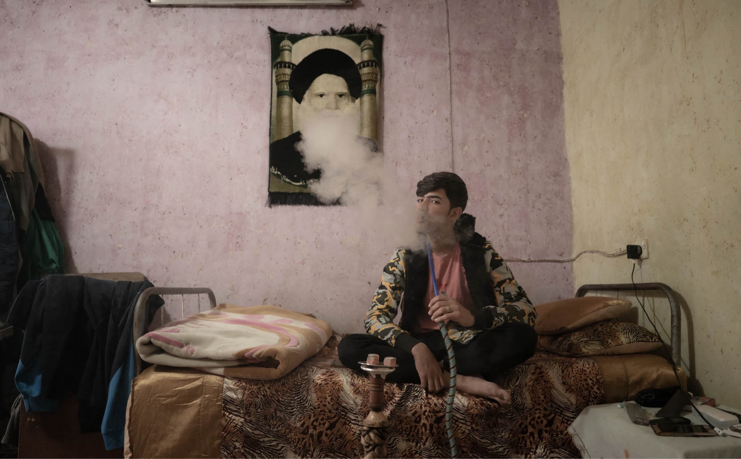 Baqir Furqan sitting on a bed smoking.