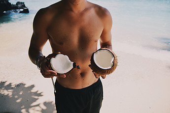 shirtless man holding coconut halves