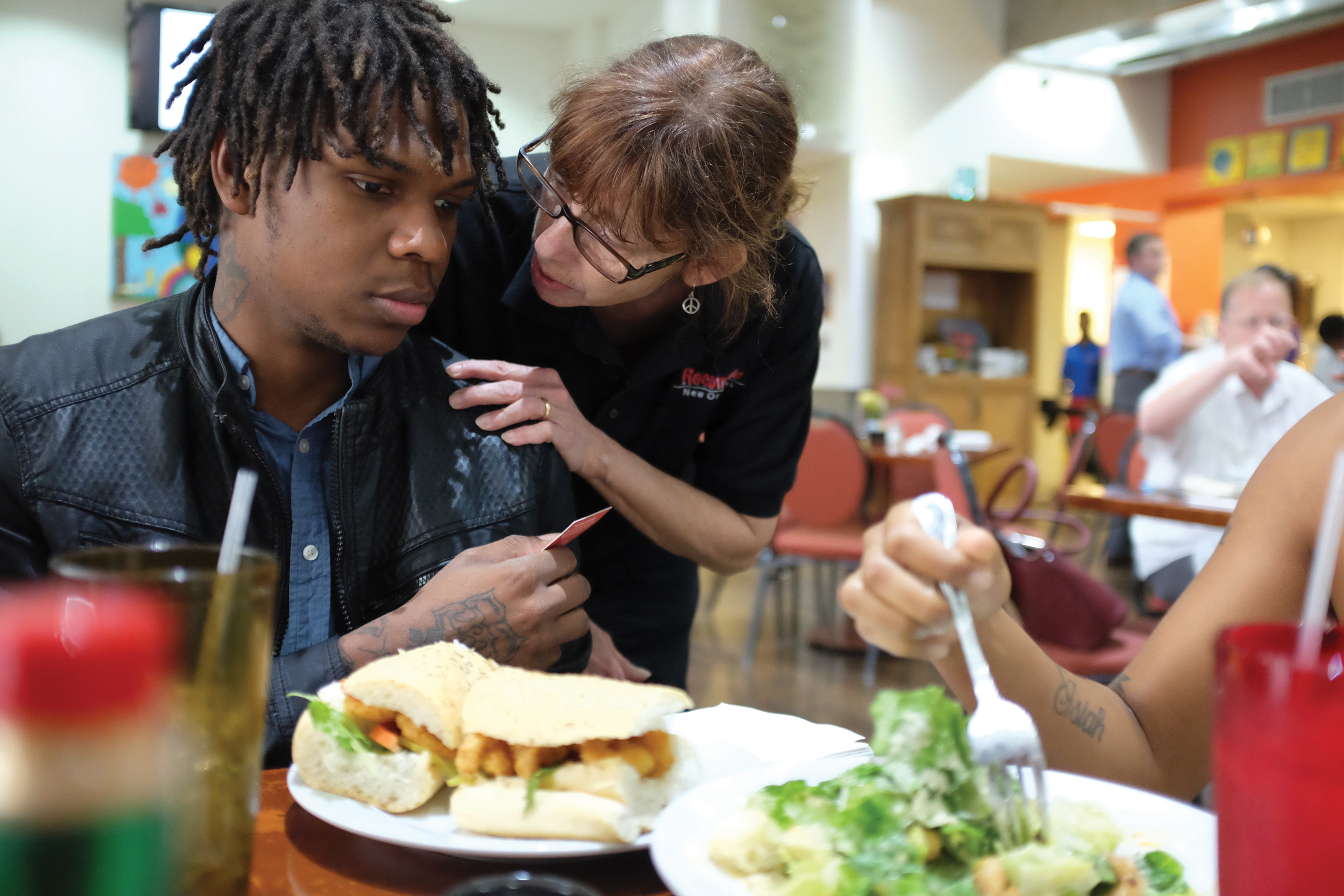 Caswick sitzt an einem Tisch, eine Restaurantangestellte fasst ihn an der Schulter und spricht zu ihm