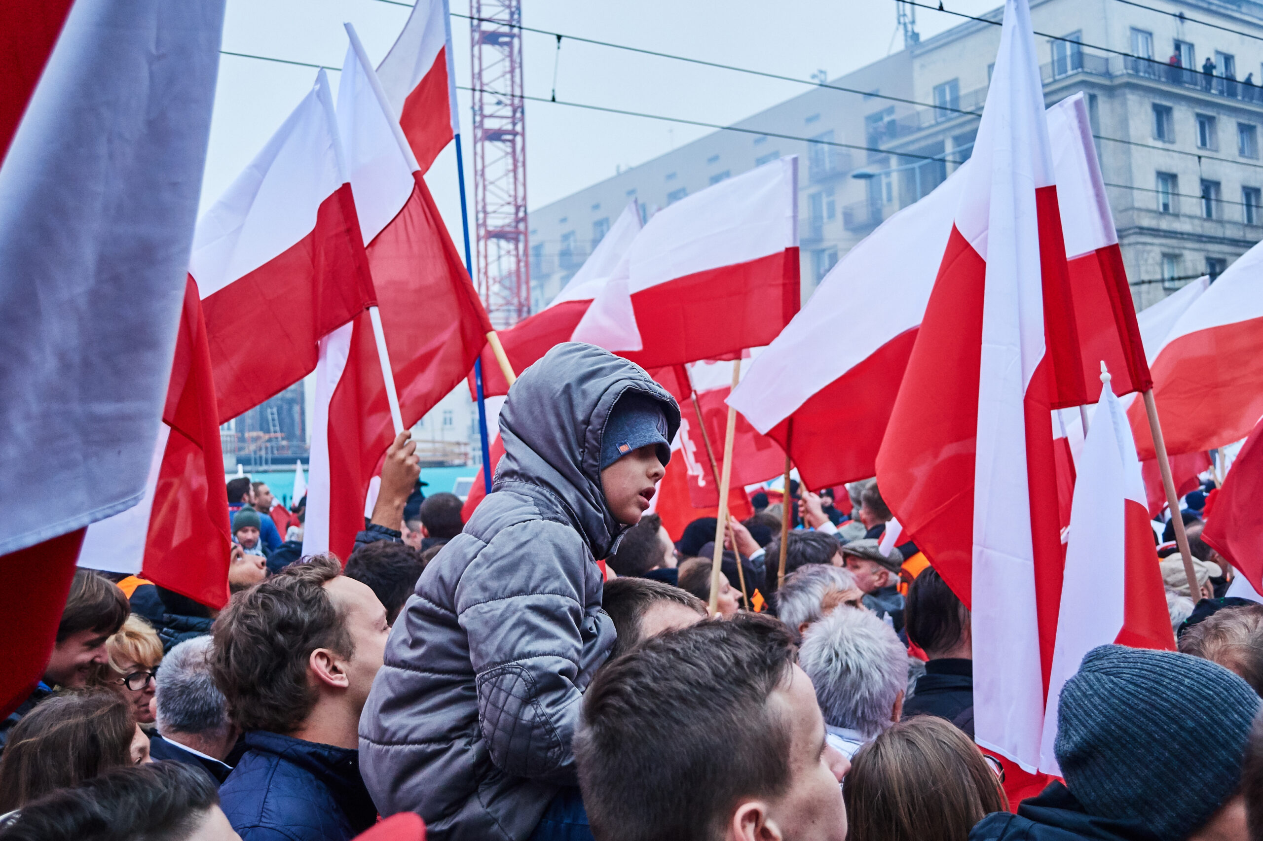 Dziecko siedzące na plecach rodzica podczas Marszu Niepodległości 2018