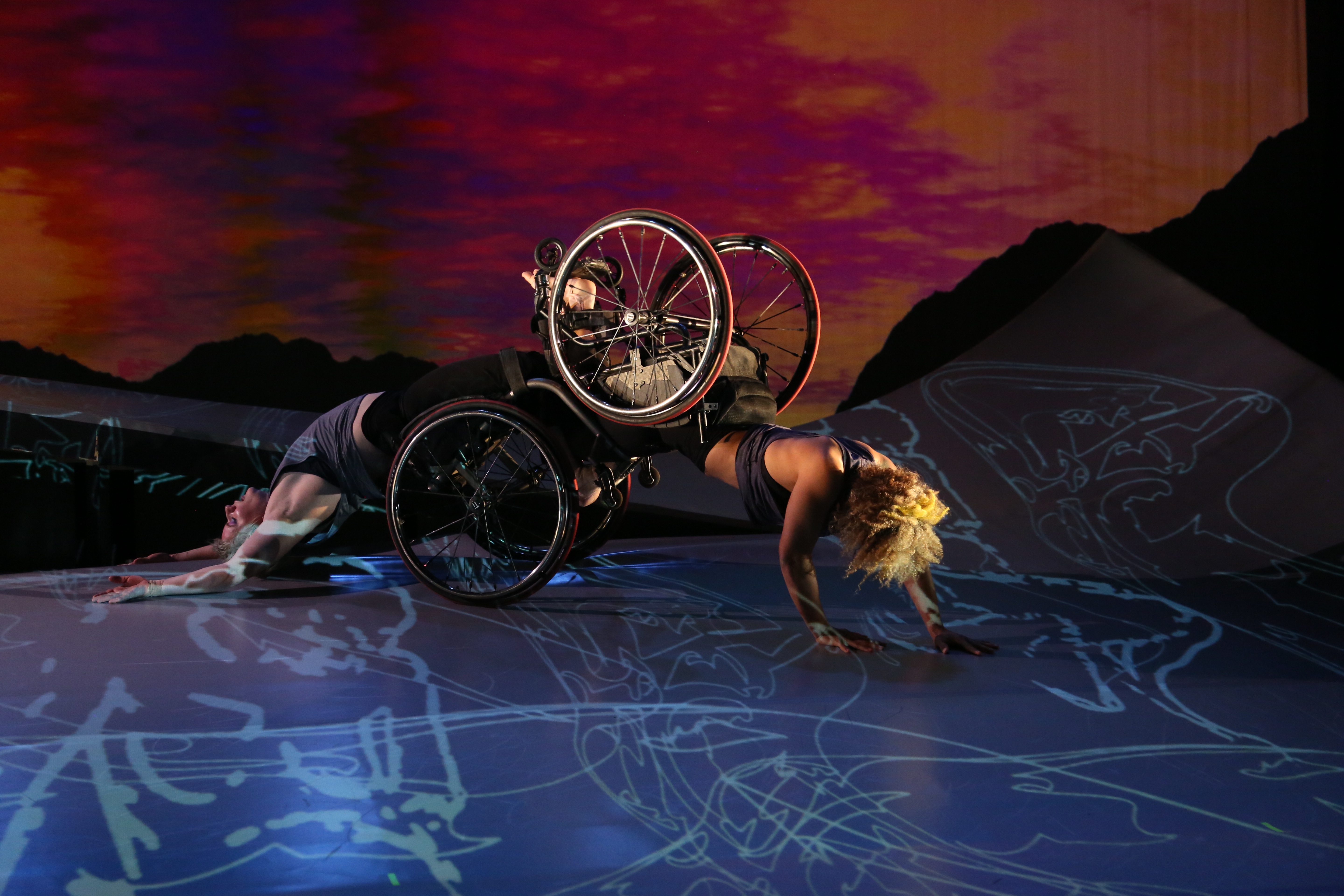 Alice Sheppard and Laurel Lawson partner, with their wheelchairs joined, at the base of the ramp in a performance of DESCENT.