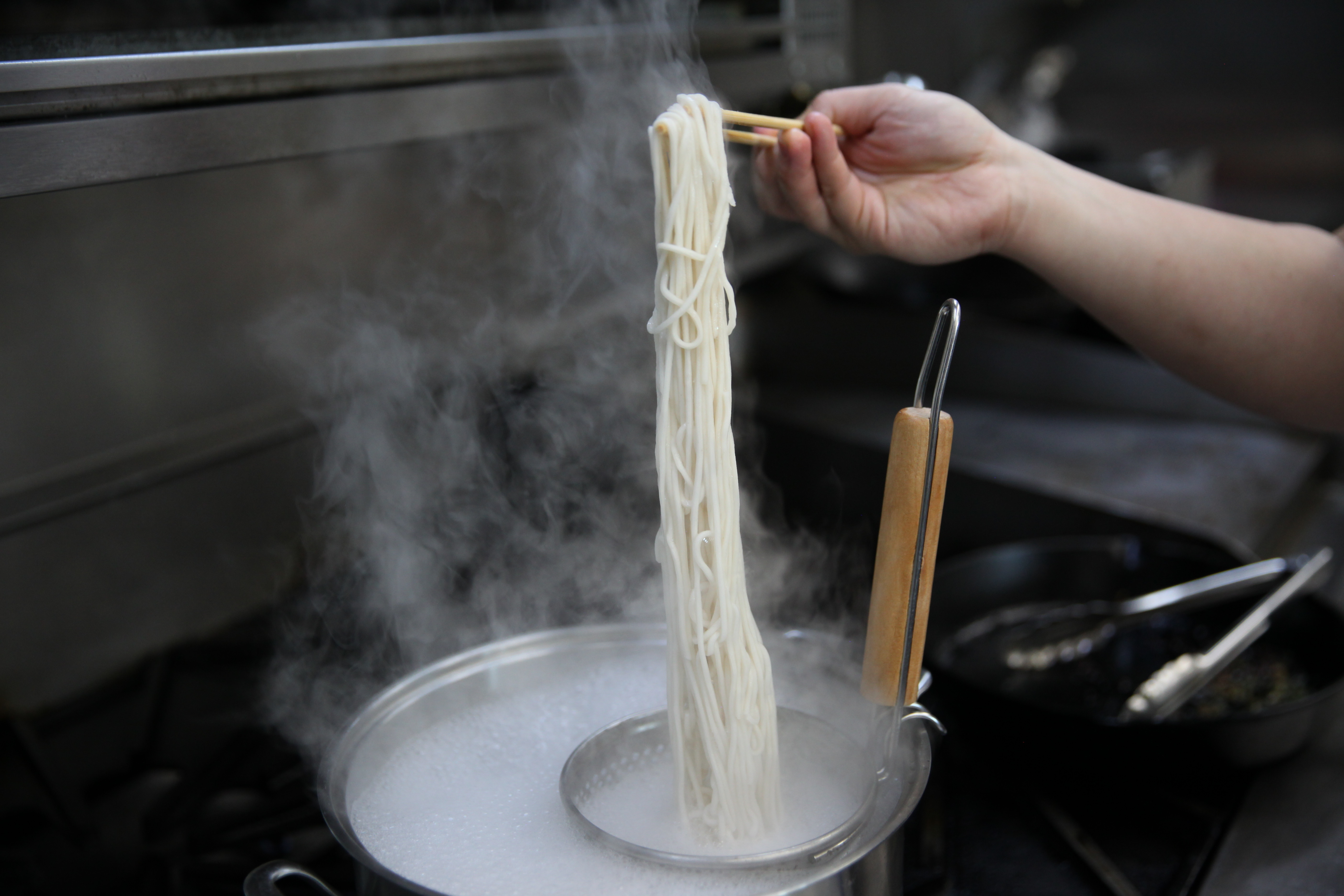 chef lucas sin holding up fresh wheat noodles above a steaming pot of water