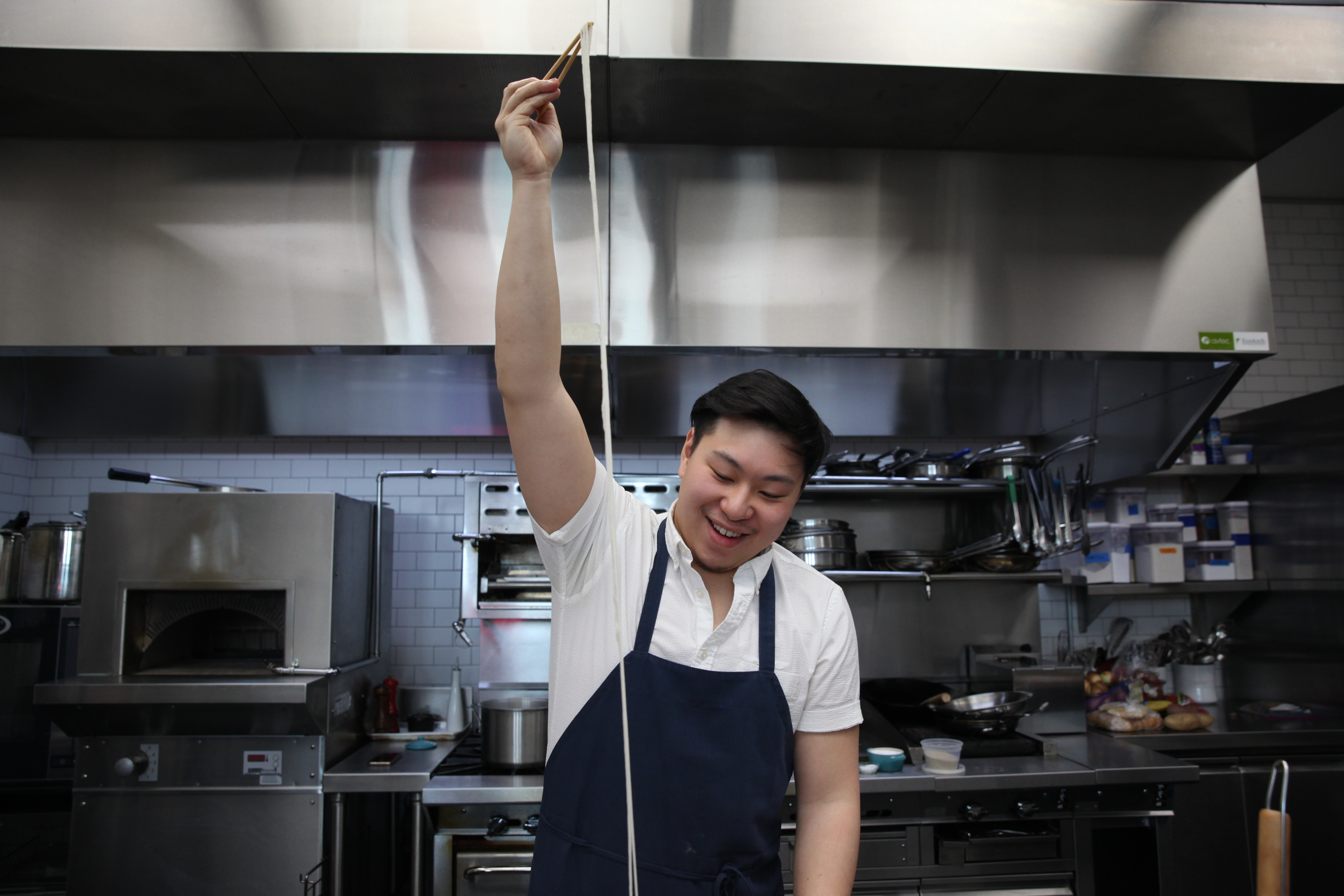 chef lucas sin of junzi kitchen holding up a long noodle using chopsticks