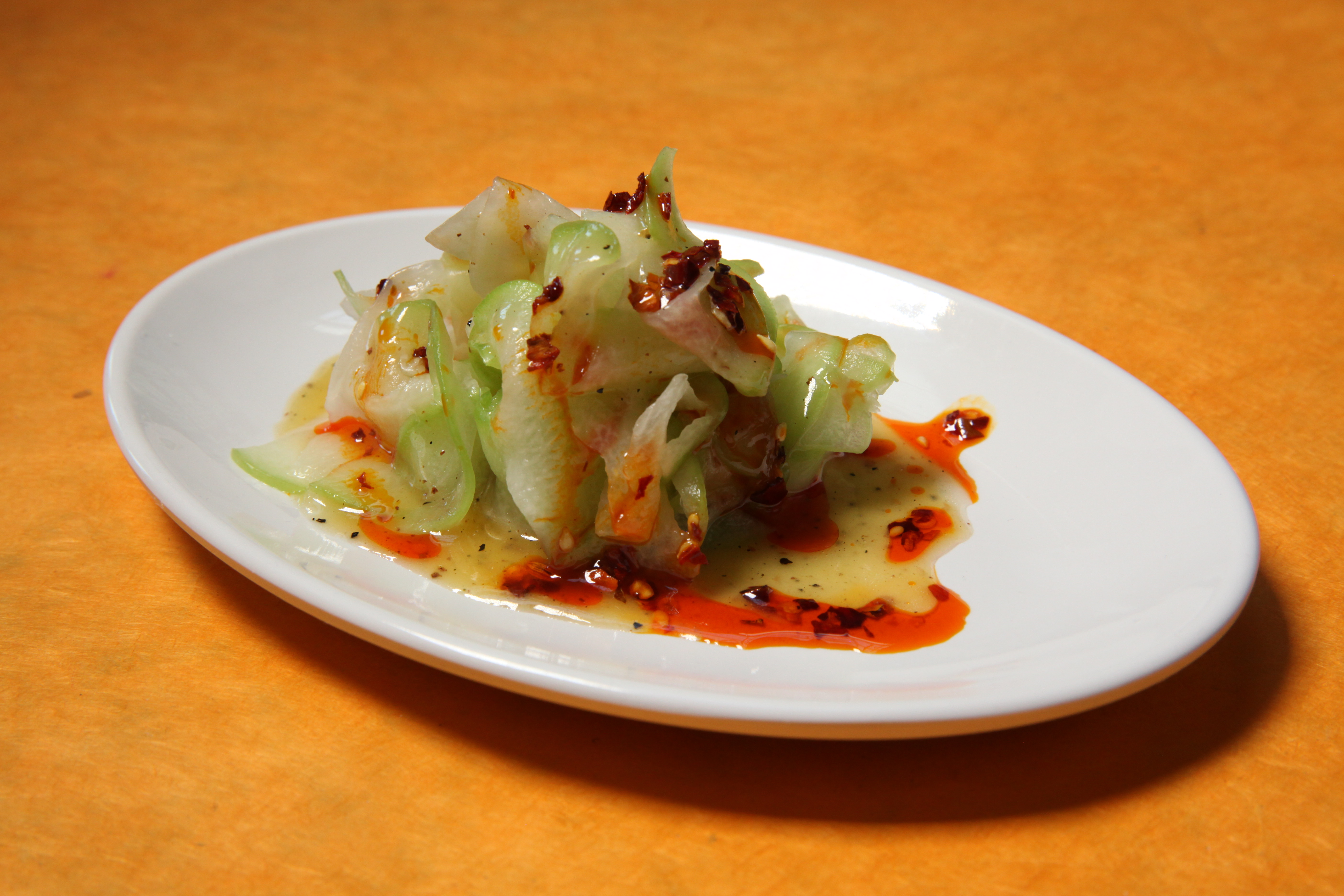 a plate of raw chayote salad with lemon curd vinaigrette and chili oil