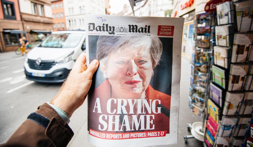 Man holding buying newspaper front page on street press kiosk newsstand with the Theresa May crying announcing resignation