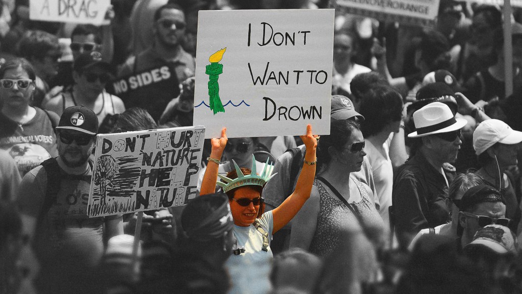A woman at a protest dressed as the Statue of Liberty holds a sign reading, "I don't want to drown."