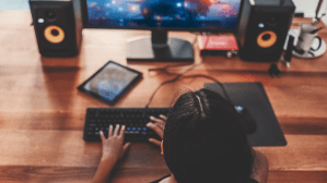 Photograph of a woman with dark skin and black hair sitting at a computer playing a video game