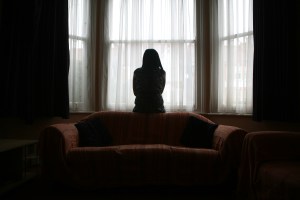 A young woman suffering from domestic violence stands in the bay window of her home. (Photo by In Pictures Ltd./Corbis via Getty Images)