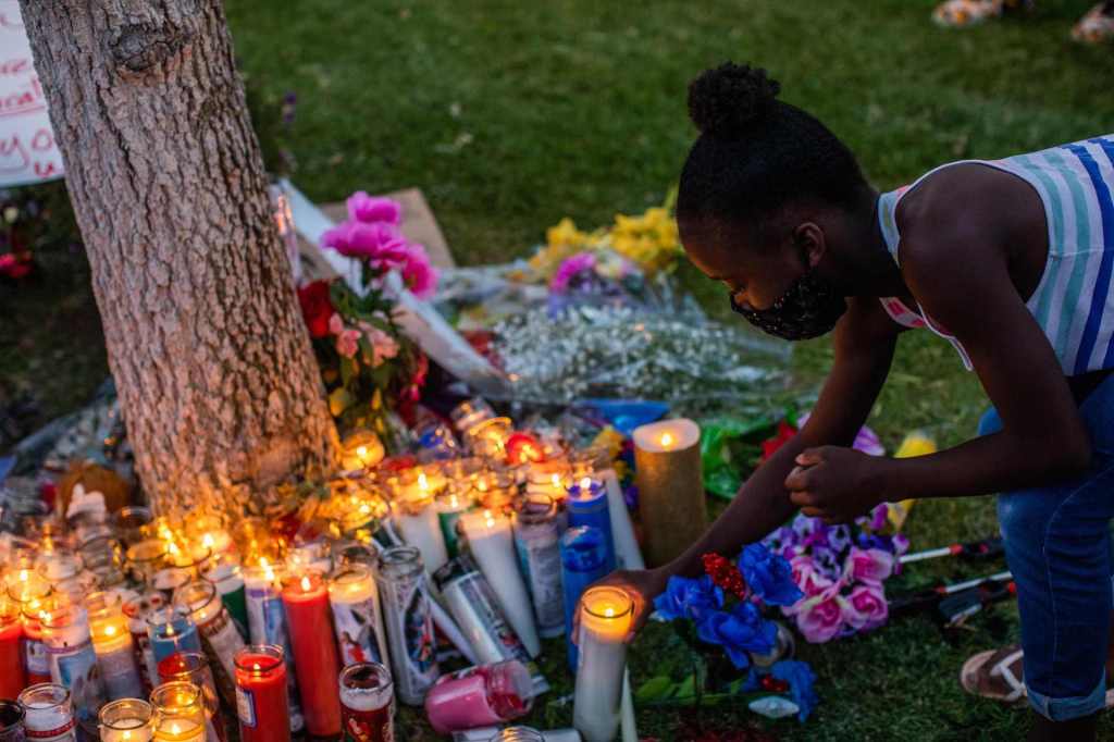 Child lights up a candle during a vigil around a makeshift memorial at the tree where Robert Fuller was found dead outside Palmdale City Hall on June 13, 2020.