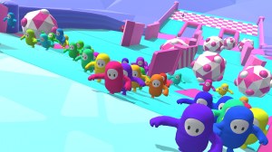 Screenshot from 'Fall Guys', Players represented as pill-shapped cartoony blobs, run up an incline as large multi-colored boulders threaten to knock them back down.
