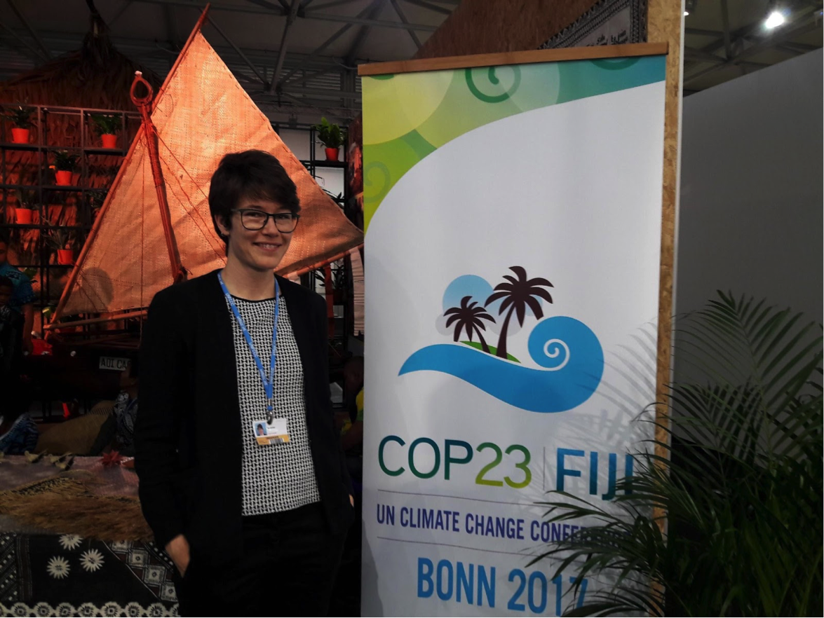 Ina Möller standing next to a banner. She has glasses and a pixie cut and is wearing a badge.