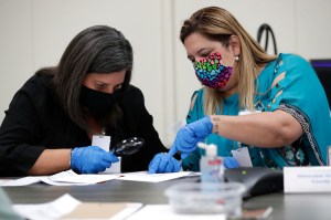 Miami-Dade County Judges Eleane Sosa-Bruzon, left, and Victoria Ferrer, right, examine signatures on vote-by-mail ballots for the August 18 primary election as the canvassing board meets at the Miami-Dade County Elections Department, Thursday, July 30, 20