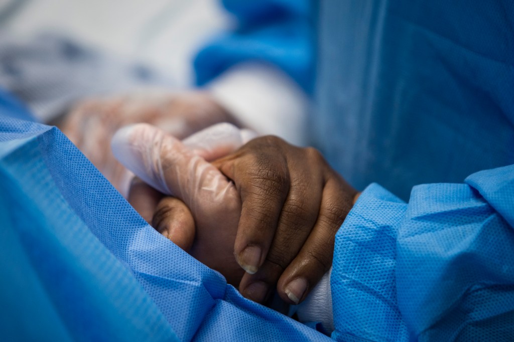 Nurse practitioner Capri Reese talks to a patient and holds her hand while a doctor administers an IV at Roseland Community Hospital in Chicago, Tuesday, April 28, 2020. (Ashlee Rezin Garcia/Chicago Sun-Times via AP)