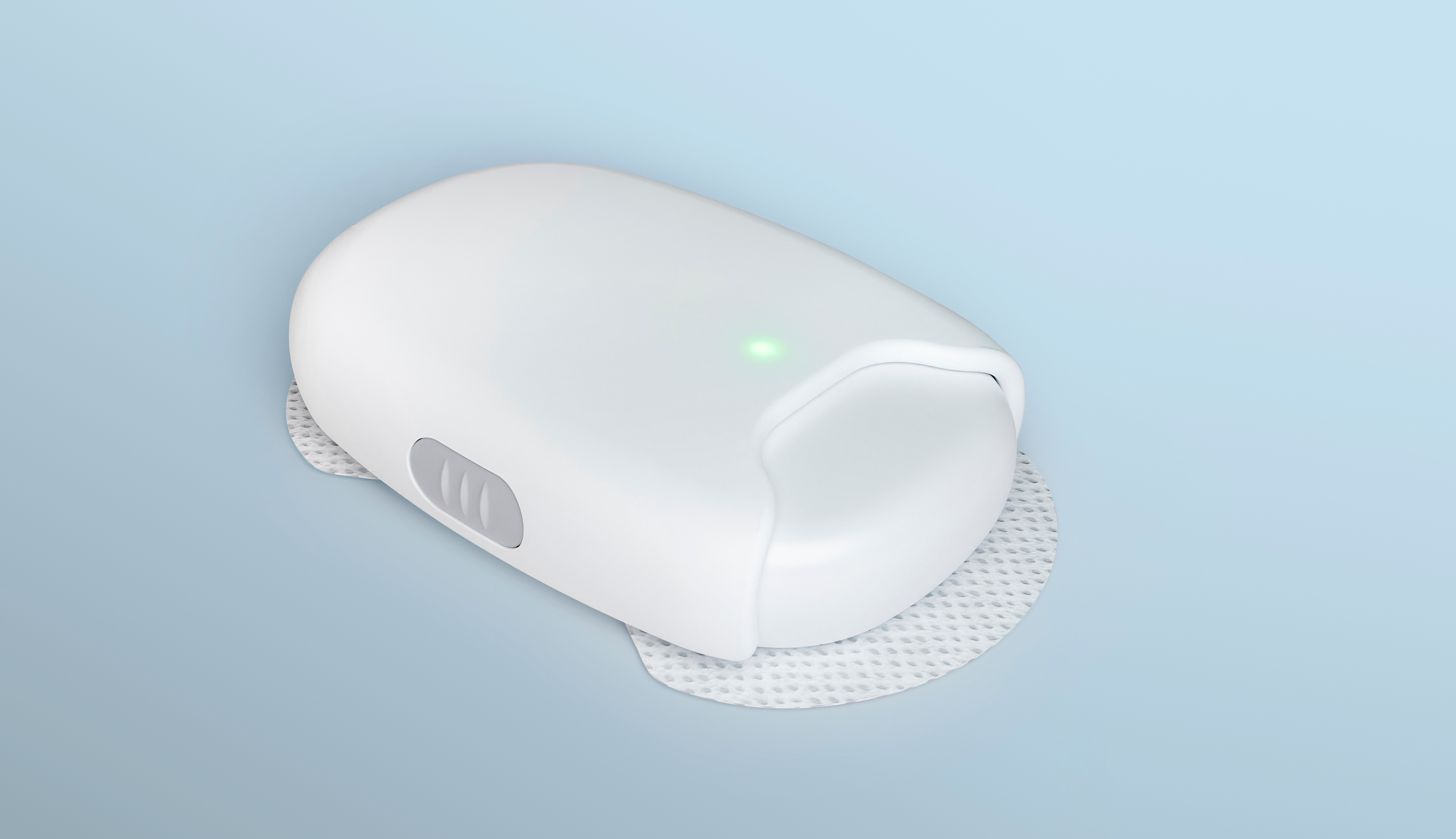 A white, oval-shaped plastic device designed to be worn on the body. The device has with a green light in the center and sterile pads on the bottom for skin contact.