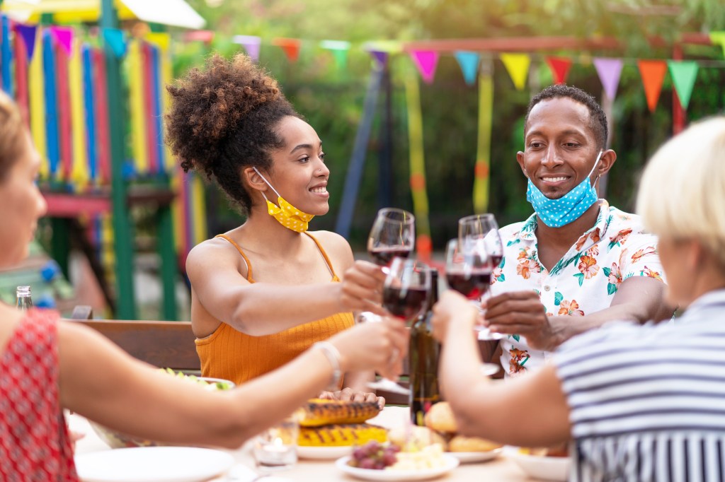 Group of friends having dinner on back yard and wearing protective face mask, during COVID-19