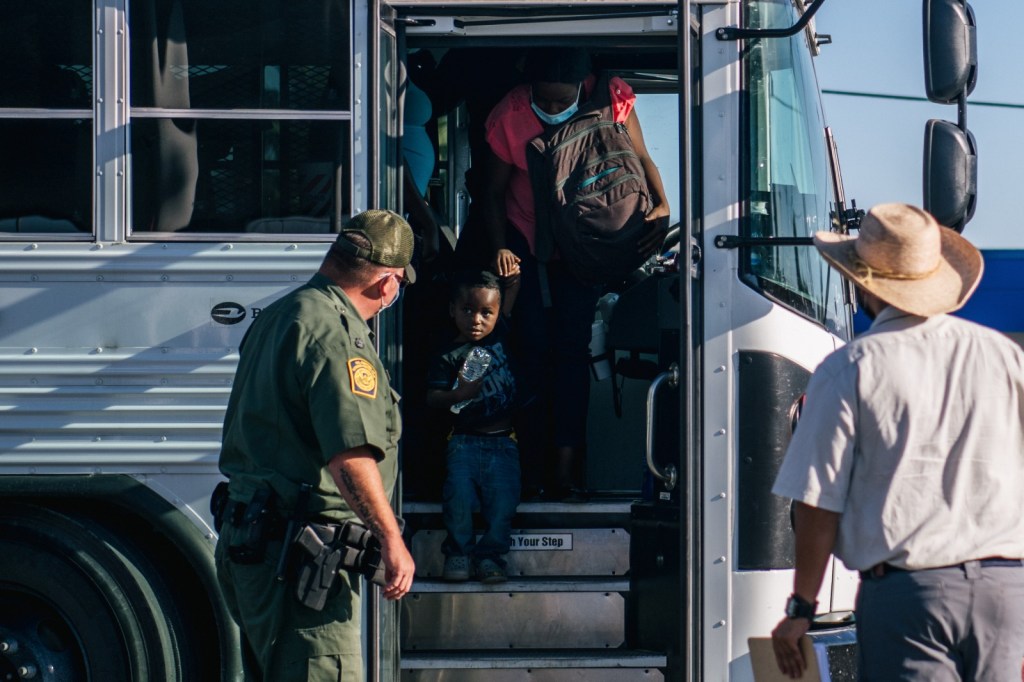 Migrants exit a Border Patrol bus and prepare to be received by the Val Verde Humanitarian Coalition after crossing the Rio Grande on September 22, 2021 in Del Rio, Texas.