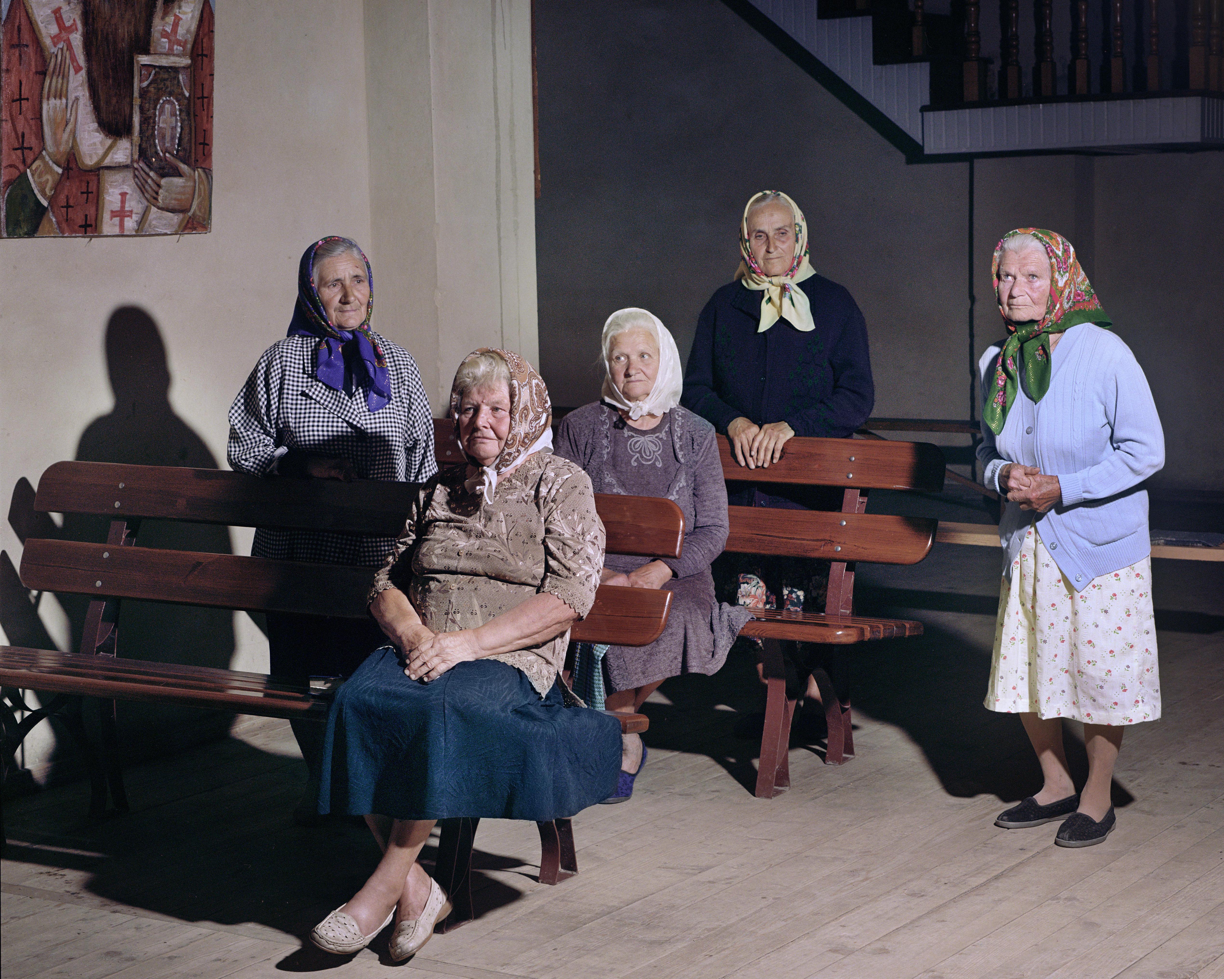 Fünf alte Frauen mit bunten Kopftüchern und Röcken sitzen und stehen in einem griechisch-katholischen Gotteshaus