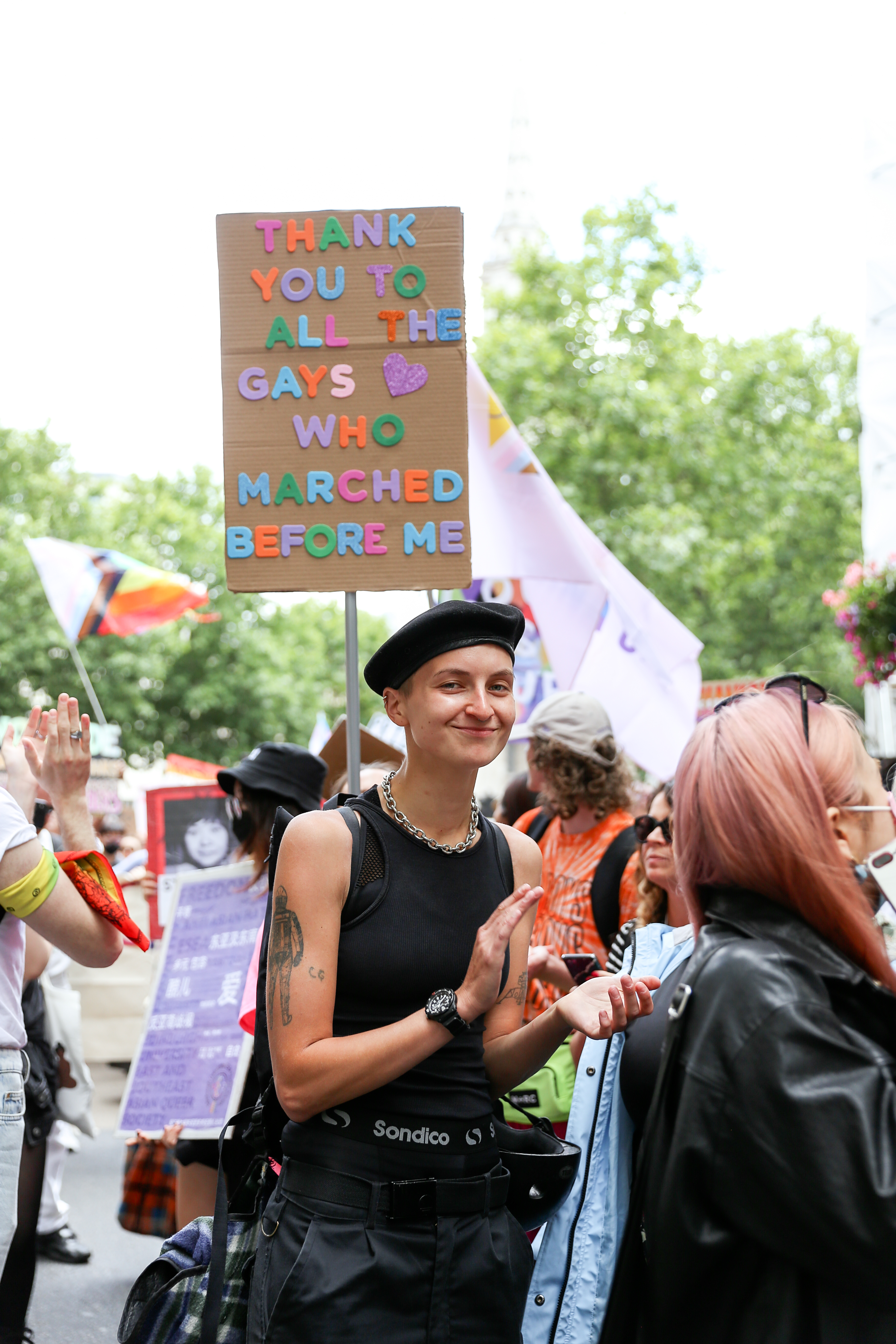 Young queer person with sign thanking older gay people
