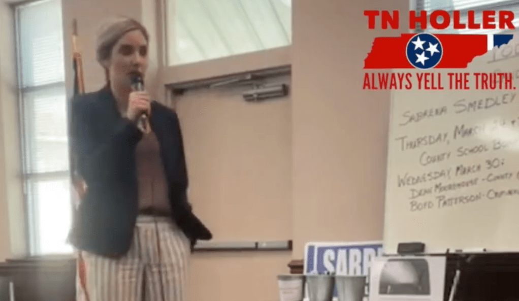 A screenshot from a video of Coty Wamp holding a microphone at a meeting with the group Moms For Liberty