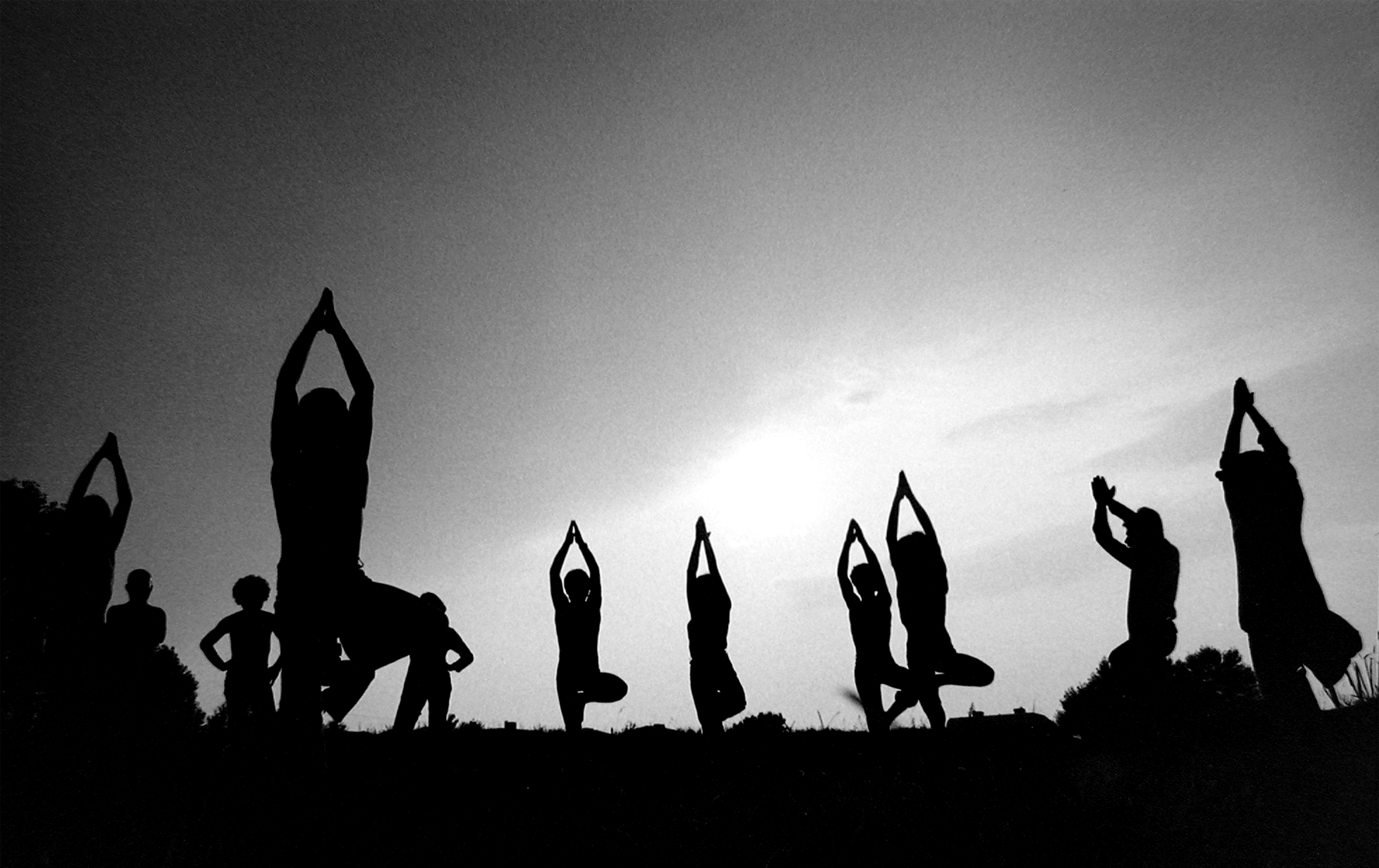 Italo Bertolasi, Italian Hippies – black and white photo showing the silhouette of people in a tree pose in a field.