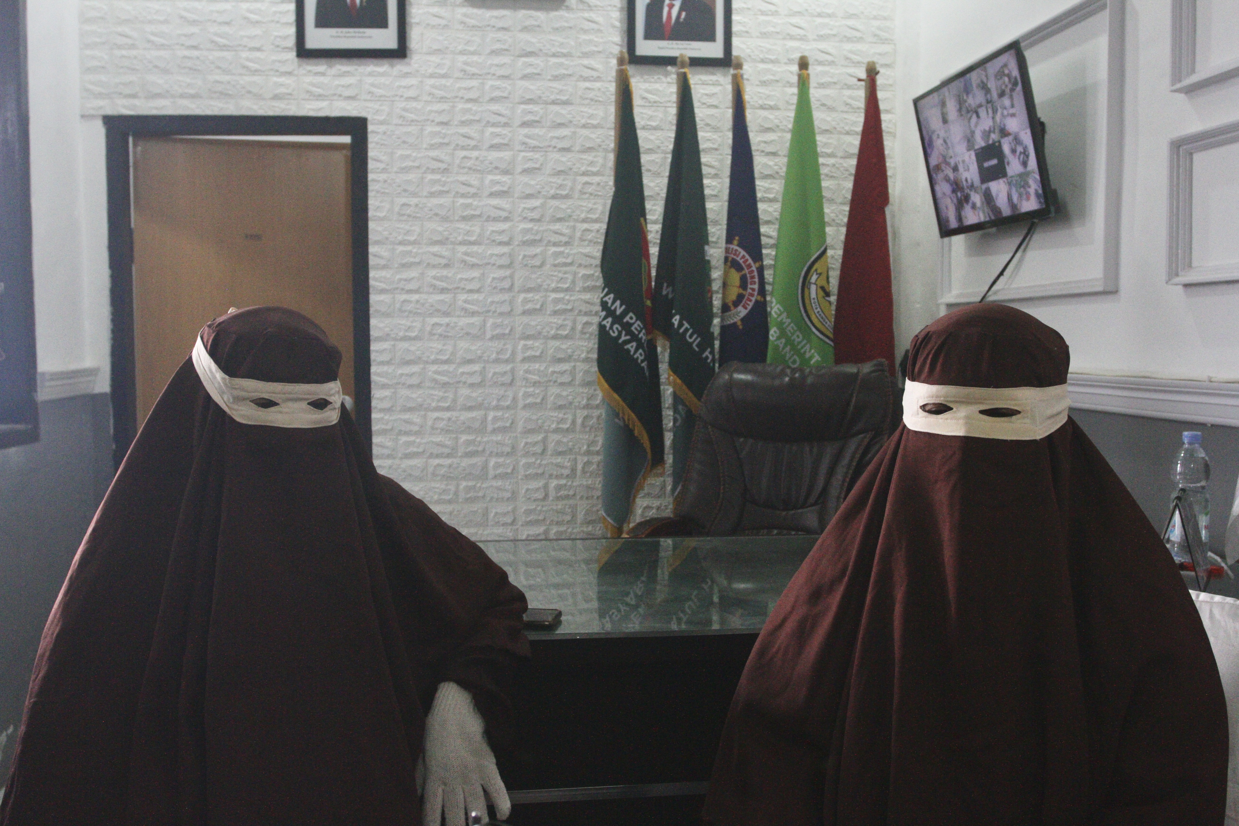 Dua perempuan mengenakan gamis dan cadar serba cokelat. Mereka pakai sarung tangan dan penutup mata putih