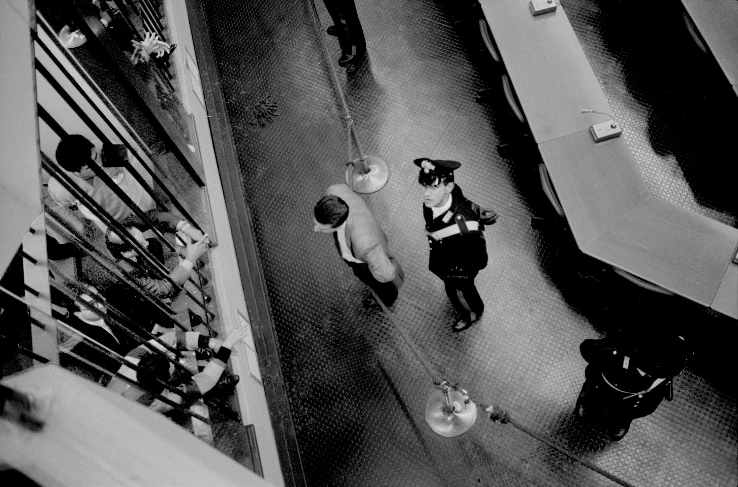 Fabio Sgroi, Seconde guerre mafieuse - photo en noir et blanc d'un carabinier regardant vers quelqu'un sur un balcon à un étage supérieur. À côté de lui, un homme en costume. Au-dessus d'eux, une foule qui attend dans une cellule.