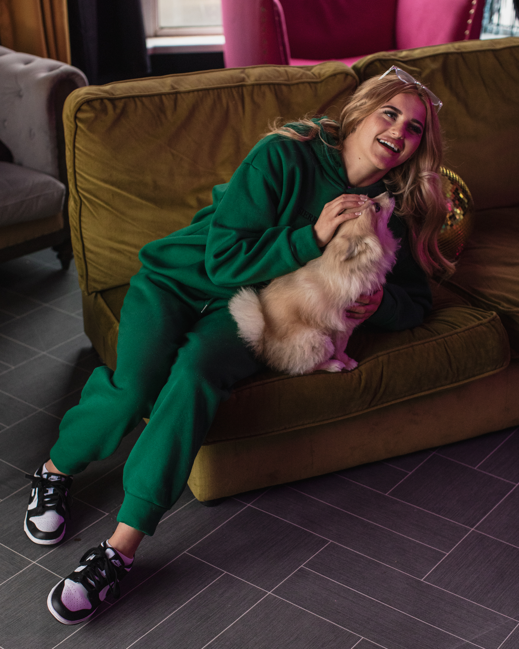 Sophie Aspin lounges on a greenish yellow couch with a small blonde dog.