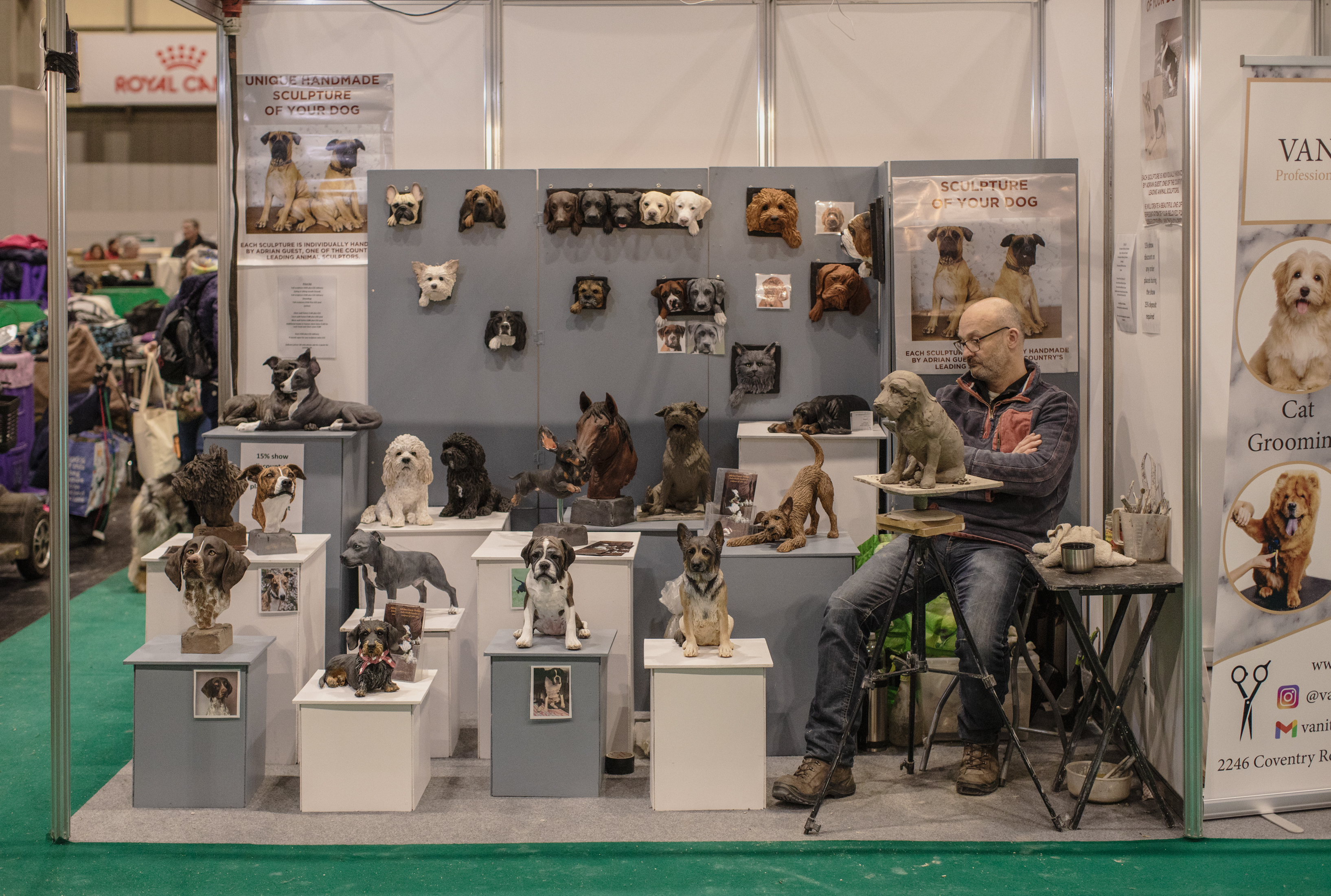 A man sits in a convention booth filled with dog statuettes on plinths.