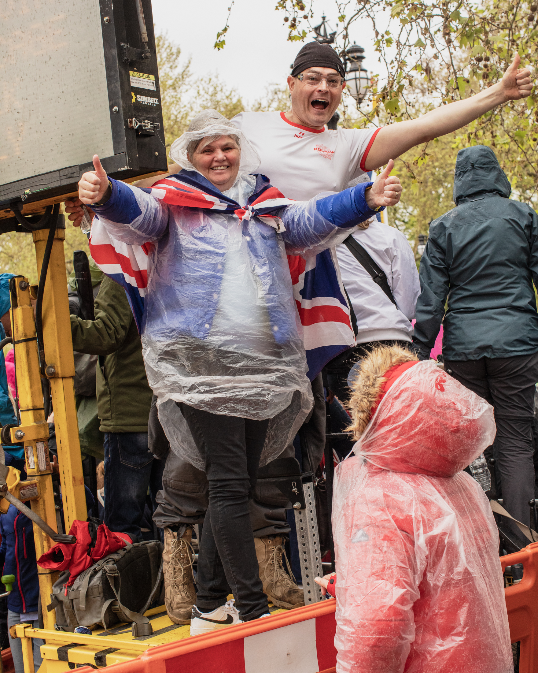 Coronation of King Charles II, London: People hold thumbs up in raincoats