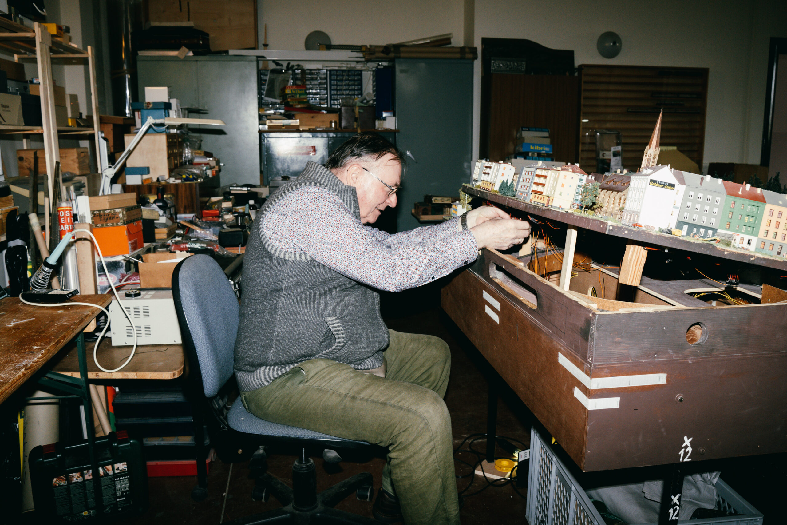 Ein Mann hebt einen Teil einer Modellbahnanlage hoch und zupft an Kabeln