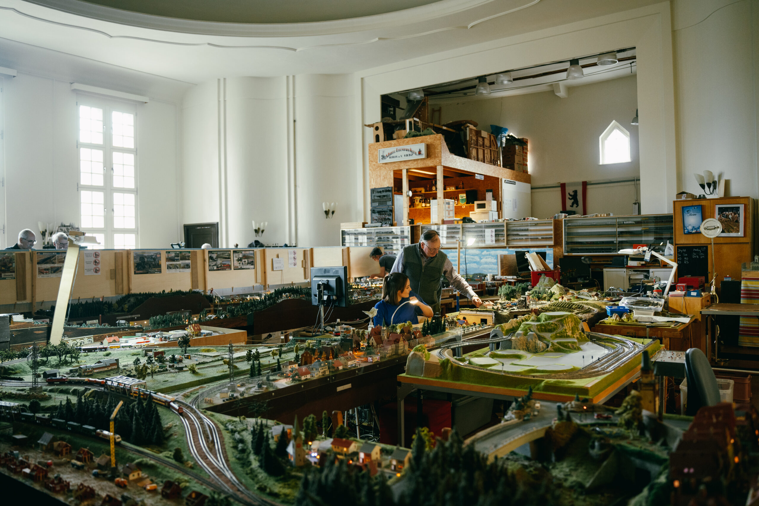 Die Autorin und ein Mann sitzen und stehen inmitten einer Modellbahnanlage